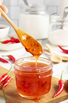 a spoon full of hot sauce on top of a wooden cutting board with red chili peppers in the background