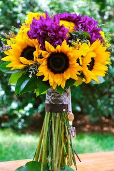 a bouquet of sunflowers and purple flowers in a vase on a wooden table