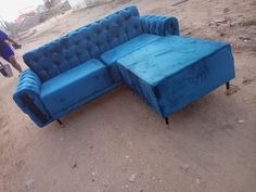 a blue couch sitting on top of a dirt field next to a person walking by