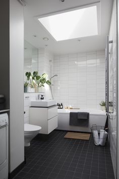 a white bathroom with black tile flooring and skylights above the bathtub, toilet and sink