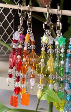 many different colored beads hanging from a white hook on a metal rod next to a plant