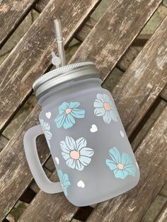 a gray and blue mason jar with flowers on it sitting on a wooden bench next to a straw