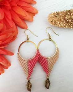 two pairs of earrings sitting on top of a white table next to orange and pink flowers