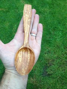 a person holding a wooden spoon in their hand on some green grass with the other hand