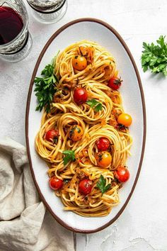 a plate of spaghetti with tomatoes and parsley next to two glasses of red wine