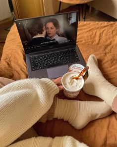 a person sitting on a bed with a laptop and cup of coffee