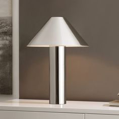 a lamp is sitting on a table next to a white dresser with drawers in the background