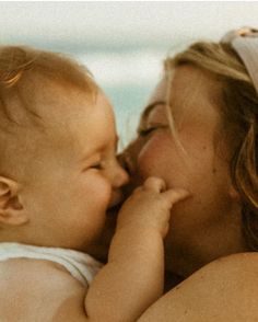 a woman kissing a baby on the beach