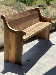 a wooden bench sitting on top of a cement floor next to a field and trees