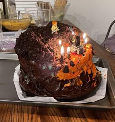 a chocolate birthday cake with lit candles sitting on top of a metal pan in front of a wooden table