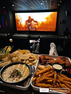 a person sitting in front of a tv watching movies with food on the table next to it