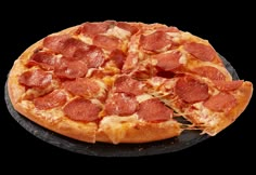 a pepperoni pizza on a black plate with one slice being taken out of it