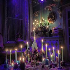 a table topped with lots of lit candles in front of a window filled with purple light