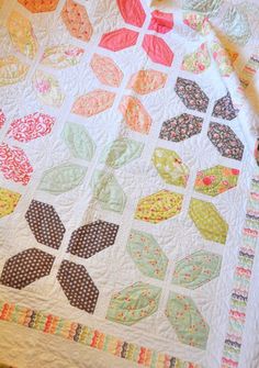 a quilt is laying on the floor next to a table topper with an orange and pink flower