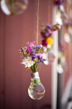 hanging vases filled with colorful flowers in front of a pink wall