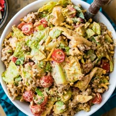 a white bowl filled with salad on top of a blue cloth next to a wooden spoon