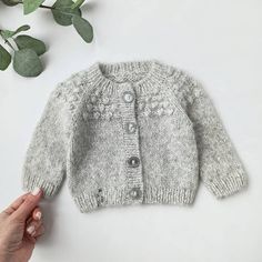 a hand is holding the top of a baby's gray cardigan sweater with buttons