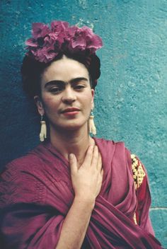 a woman in a red dress with flowers on her head standing against a blue wall