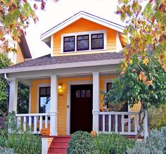 a yellow house with two pumpkins on the front porch