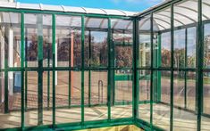 the inside of a green house with glass walls and doors on both sides, looking out onto a tennis court