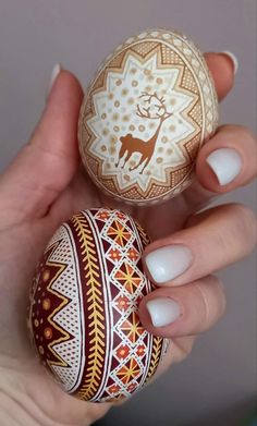 a woman holding two decorated eggs in her hands, one painted with an image of a deer