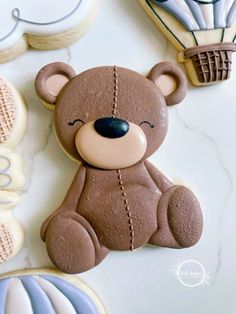 a teddy bear cookie sitting on top of a table next to cookies and hot air balloons