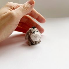 a tiny stuffed animal being held by someone's hand on a white table top