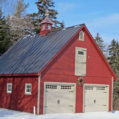 a red barn with two garages and a steeple on the roof is surrounded by snow