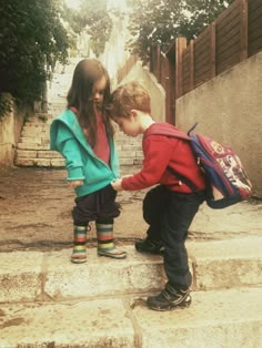 two young children standing on steps with backpacks over their shoulders and one holding the other's hand