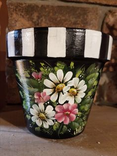 a painted flower pot sitting on top of a table next to a stone wall with black and white stripes