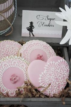 pink and white cookies in a box with lace doily on them, next to a card