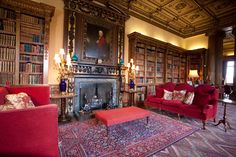 a living room filled with red couches and lots of books on the shelves next to a fire place