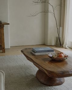 a wooden table with a bowl of fruit on it in front of a tree branch