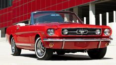 an old red mustang parked in front of a building