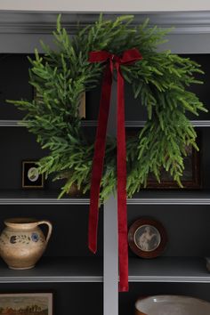 a christmas wreath on top of a bookcase with a red ribbon tied around it