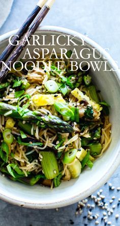 a bowl filled with noodles, asparagus and other vegetables next to chopsticks