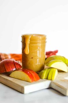 a jar of apple butter sitting on top of a cutting board next to sliced apples