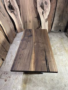 a table made out of wood sitting on top of a cement floor next to stacks of wooden planks