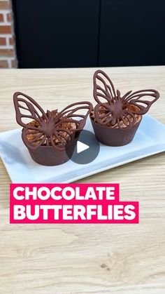 two chocolate butterflies sitting on top of a white plate next to a cupcake covered in frosting