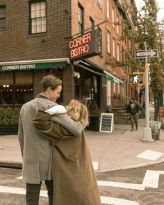 a man and woman crossing the street in front of a corner bistro with their arms around each other