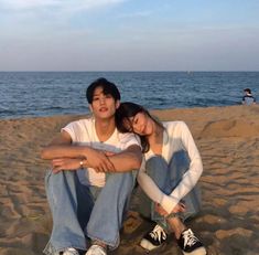 two people are sitting on the beach talking on their cell phones and smiling at each other