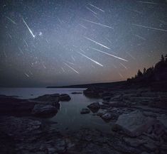 the night sky is filled with stars and shooting comets in the distance over water