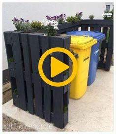 two trash cans sitting next to each other on the side of a building with flowers growing out of them