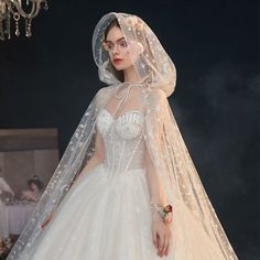 a woman in a white wedding dress with a veil on her head is standing next to a chandelier