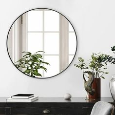 a round mirror on the wall above a desk with a chair and potted plant