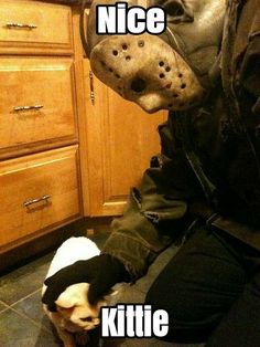 a person wearing a mask sitting on the floor next to a dog in a kitchen