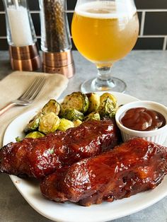 a plate with ribs and brussel sprouts next to a glass of beer