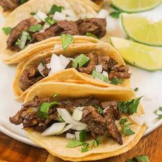 three tacos on a plate with limes and cilantro