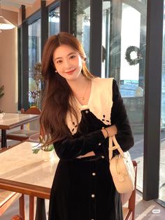 a woman standing in front of a table holding a white purse and smiling at the camera