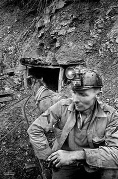 black and white photograph of a man sitting in front of a tunnel on the side of a mountain